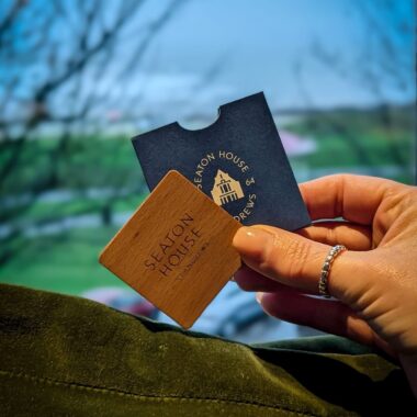 Seaton House St Andrews room key and wooden key card with coastal view in background.