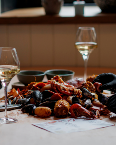 Two diners wearing lobster bibs and black gloves sharing a seafood boil with Scottish shellfish and glasses of white wine at Dulse Leith.